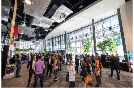 Groups of professionals gathered in spacious atrium with natural light and modern architecture.