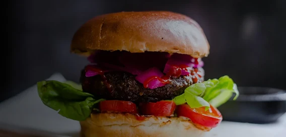 Close-up of a gourmet burger with lettuce, tomato, and pickled onions.