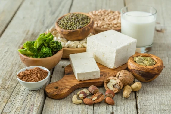 Tofu, legumes, nuts, seeds, broccoli, and a glass of plant-based milk on a wooden table.