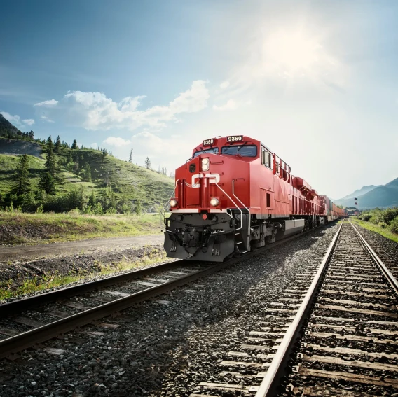 Red freight train traveling on tracks through a mountain landscape on a sunny day.