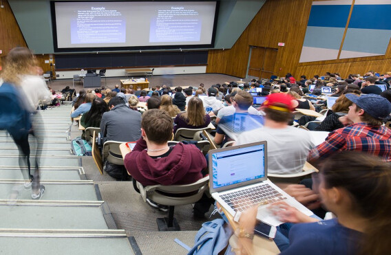 Large lecture hall filled with students using laptops and notebooks