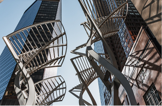 Metal spiral sculptures between tall glass skyscrapers in city center.