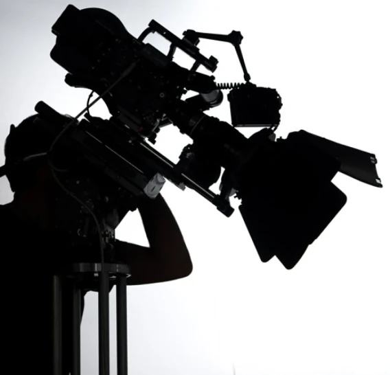 Silhouette of a professional cinema camera and operator against a bright white background.