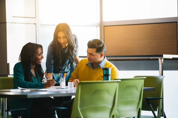 Three coworkers collaborating at a table in a modern office meeting space.