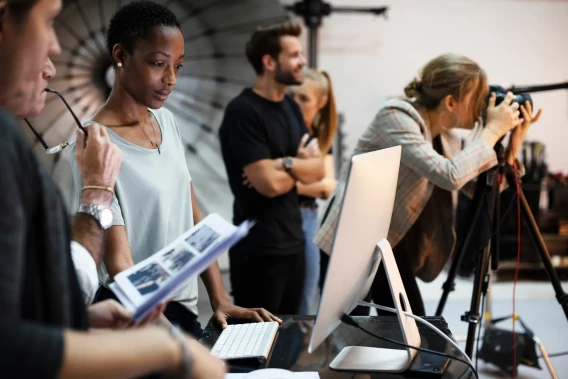 Creative team reviewing images at a workstation while a photographer works in a studio.