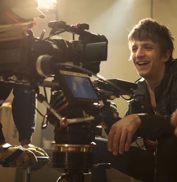 Smiling filmmaker crouched beside a professional cinema camera during production.