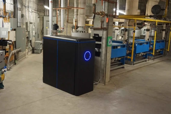 Industrial utility room with equipment, pipes, and a black energy system unit in the foreground.