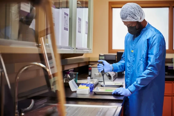 Lab technician in protective clothing pipetting samples inside a controlled cleanroom.