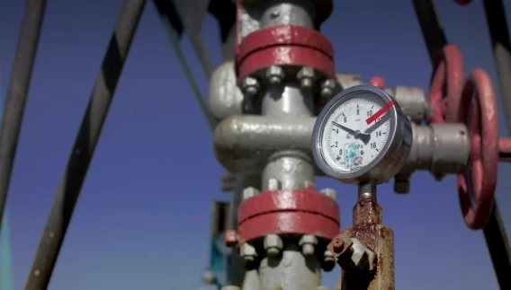 Close-up of a pressure gauge mounted on oil well equipment against a clear blue sky.
