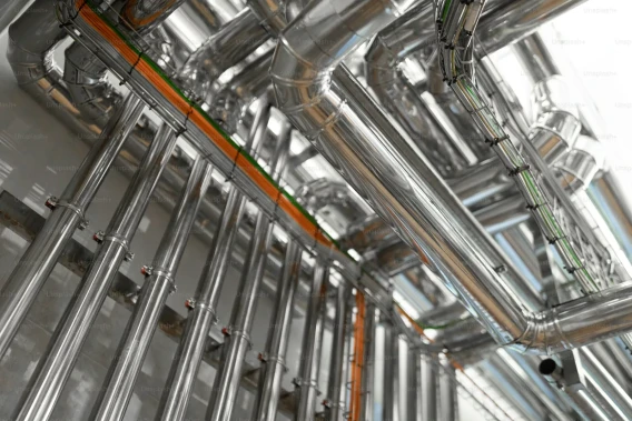 Close-up view of a stainless steel industrial piping network with reflective ducts and cable runs.