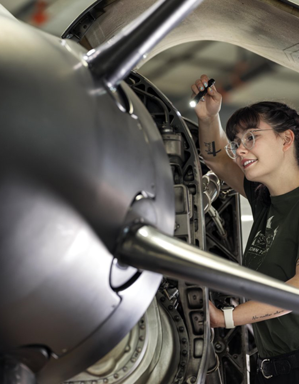 Technician examining aircraft engine components with flashlight in hangar workshop