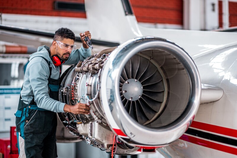 Technician inspecting a jet engine on a small aircraft inside a maintenance hangar.