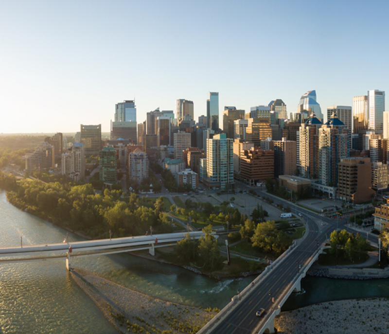 Aerial view of modern downtown skyscrapers, riverfront green spaces, and bridges at sunset.