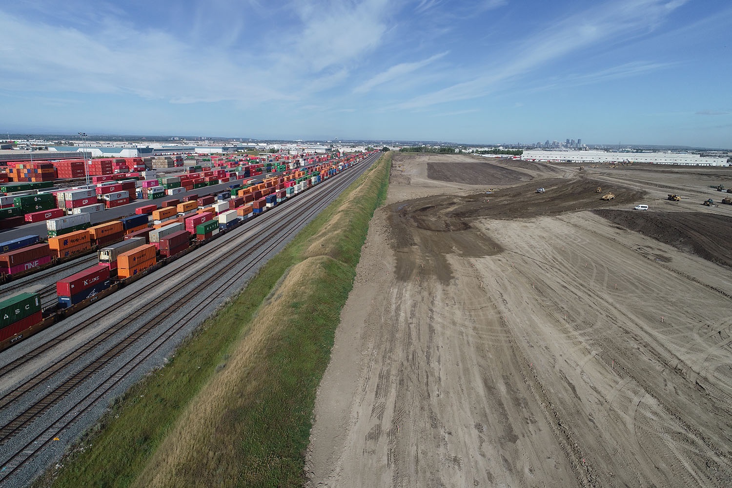 Industrial rail yard with stacked containers and construction site nearby.